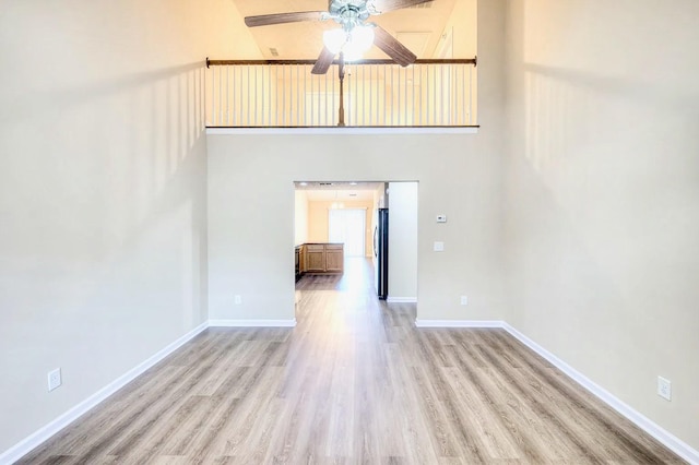 unfurnished living room featuring a high ceiling, ceiling fan, and light wood-type flooring