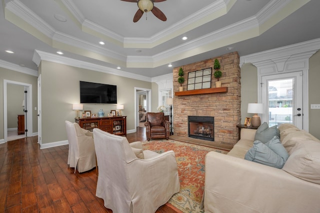 living room featuring ceiling fan, dark hardwood / wood-style floors, crown molding, a tray ceiling, and a fireplace