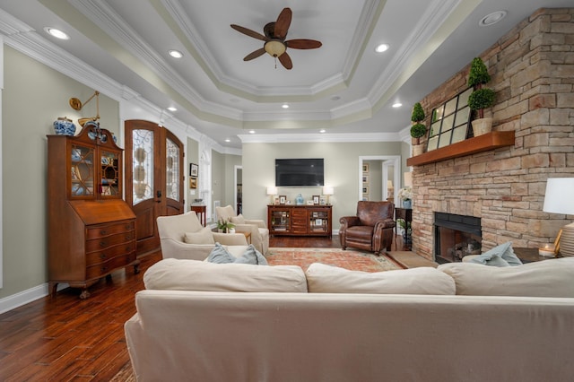 living room with ceiling fan, a raised ceiling, dark hardwood / wood-style flooring, crown molding, and a fireplace