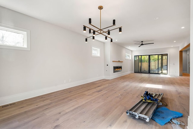 unfurnished living room featuring ceiling fan with notable chandelier and light hardwood / wood-style floors