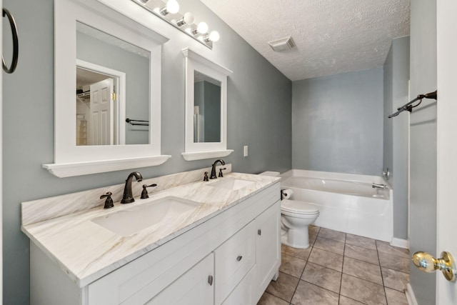 bathroom featuring a bathing tub, tile patterned flooring, vanity, toilet, and a textured ceiling