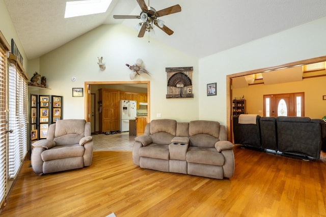 living room featuring ceiling fan, lofted ceiling with skylight, and light hardwood / wood-style flooring