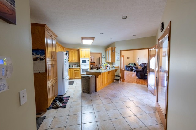 kitchen with a breakfast bar area, white appliances, light tile patterned flooring, a textured ceiling, and sink