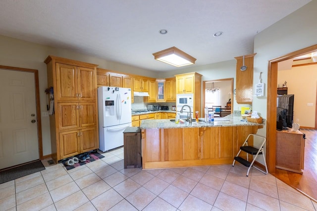 kitchen with kitchen peninsula, white appliances, light tile patterned flooring, light stone counters, and sink