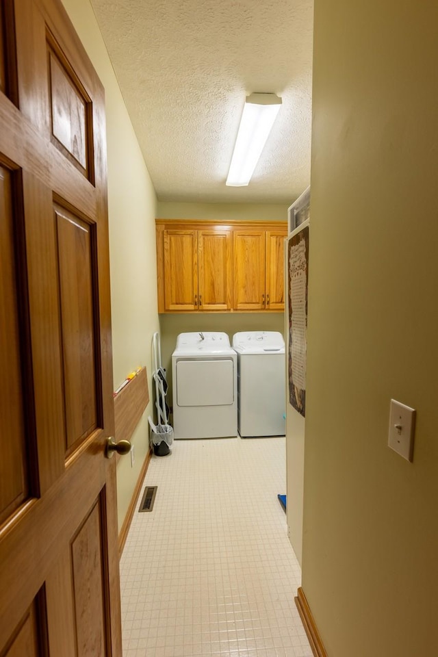 clothes washing area with a textured ceiling, separate washer and dryer, and cabinets