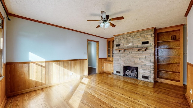 unfurnished living room featuring light hardwood / wood-style floors, a textured ceiling, ornamental molding, and a stone fireplace