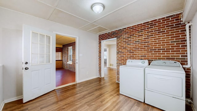 clothes washing area with separate washer and dryer, light hardwood / wood-style flooring, and brick wall