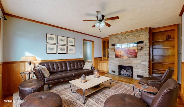 living room with a textured ceiling, a fireplace, ornamental molding, light wood-type flooring, and ceiling fan