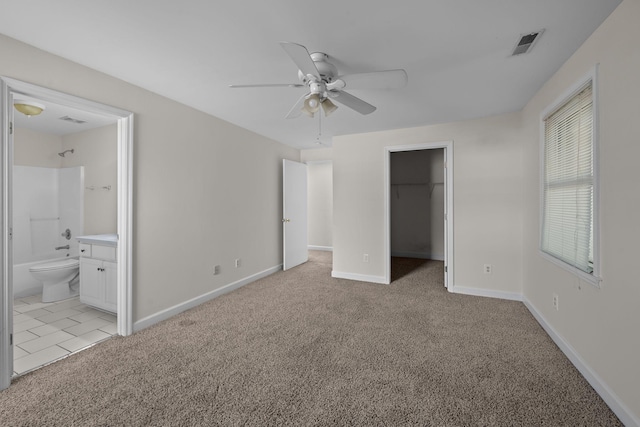 unfurnished bedroom with light carpet, ensuite bathroom, ceiling fan, a spacious closet, and a closet