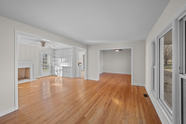 unfurnished living room featuring built in shelves, ceiling fan, and light wood-type flooring