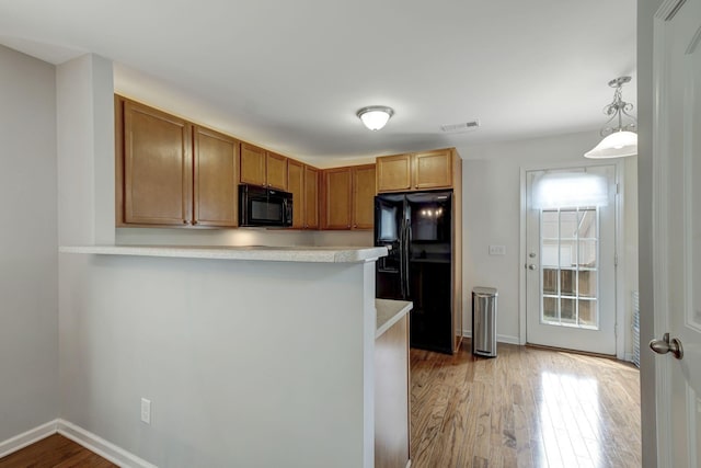 kitchen featuring kitchen peninsula, hanging light fixtures, black appliances, and light hardwood / wood-style flooring