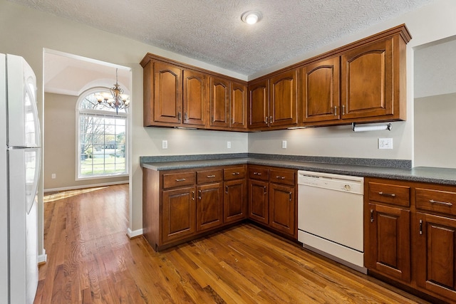 kitchen with dark wood-style floors, an inviting chandelier, dark countertops, white appliances, and brown cabinetry