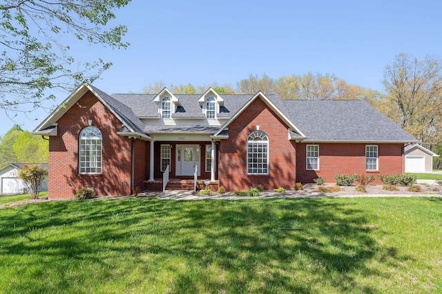 view of front of property featuring brick siding, an outbuilding, a shingled roof, and a front yard