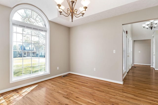 unfurnished room with light wood-style flooring, a notable chandelier, and a healthy amount of sunlight