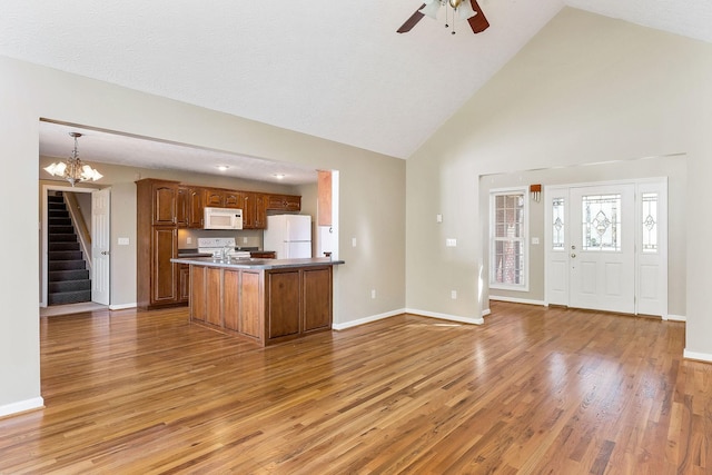 kitchen featuring high vaulted ceiling, brown cabinetry, white appliances, light wood-style flooring, and baseboards