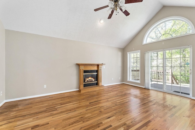 unfurnished living room with a glass covered fireplace, a ceiling fan, wood finished floors, and high vaulted ceiling