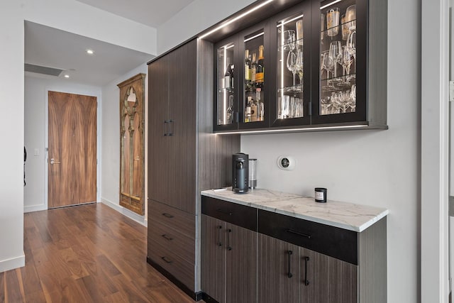 bar featuring dark brown cabinetry, light stone counters, and dark hardwood / wood-style floors