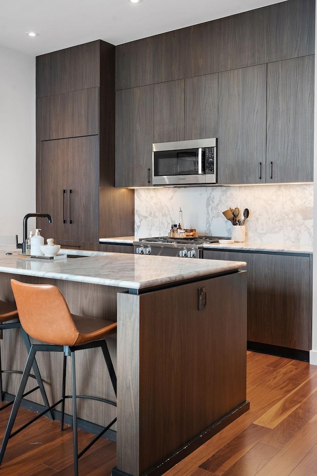 kitchen with a kitchen breakfast bar, light wood-type flooring, backsplash, dark brown cabinets, and range