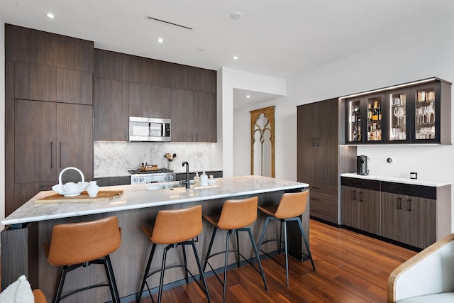 kitchen featuring backsplash, a kitchen island with sink, a kitchen bar, and dark hardwood / wood-style floors