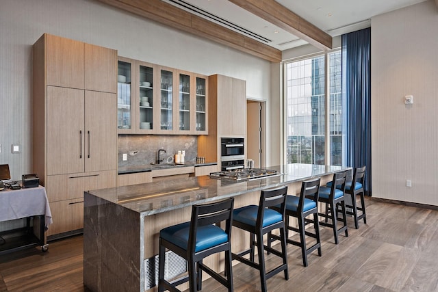 kitchen featuring a kitchen breakfast bar, oven, dark stone countertops, beam ceiling, and stainless steel gas cooktop