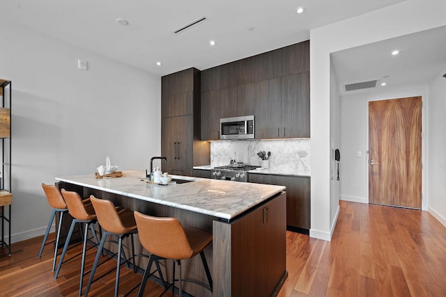 kitchen featuring sink, an island with sink, light hardwood / wood-style floors, range, and a breakfast bar area