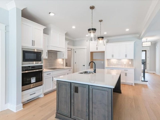 kitchen with built in microwave, stainless steel oven, sink, a kitchen island with sink, and white cabinets