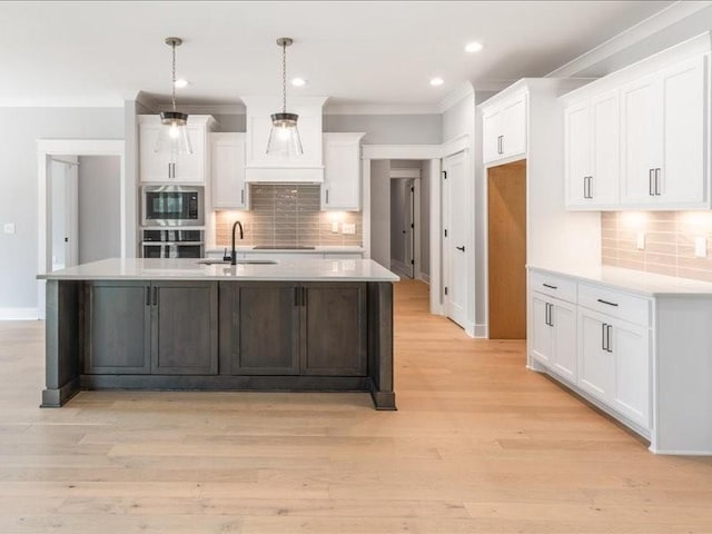 kitchen with pendant lighting, oven, sink, an island with sink, and white cabinetry