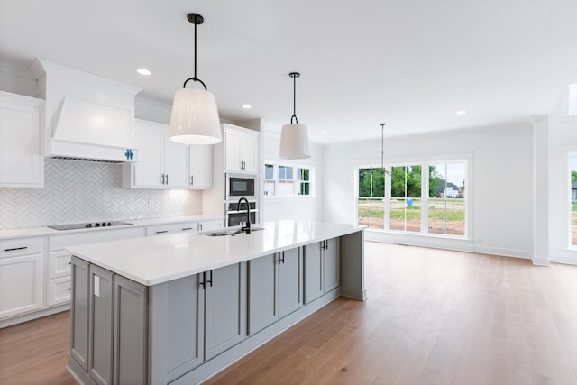 kitchen featuring sink, white cabinetry, an island with sink, and built in microwave