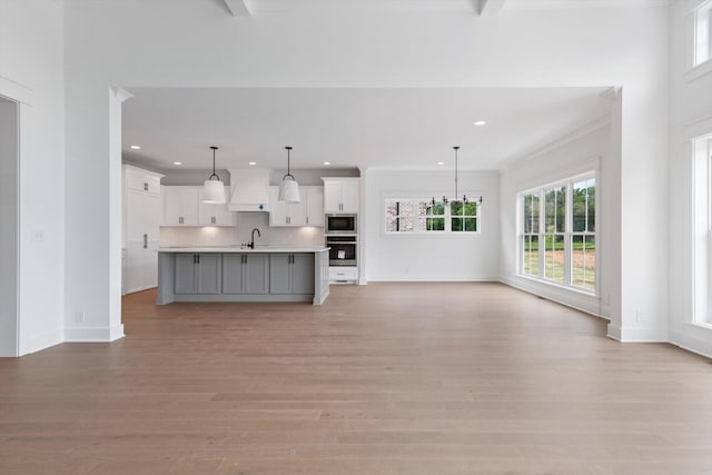 unfurnished living room with beam ceiling, light wood-type flooring, and sink