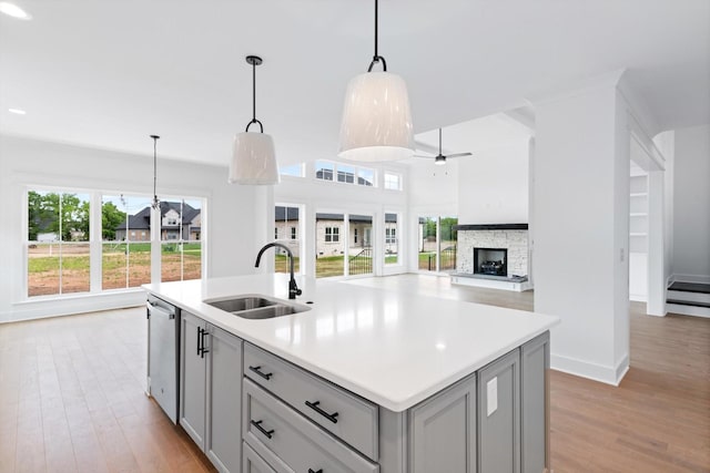 kitchen with gray cabinetry, a kitchen island with sink, hanging light fixtures, sink, and stainless steel dishwasher