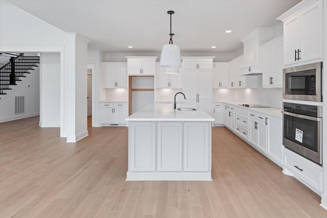 kitchen with stainless steel oven, sink, built in microwave, decorative light fixtures, and white cabinetry