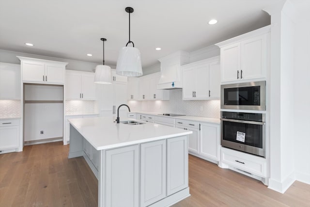 kitchen with sink, hanging light fixtures, a kitchen island with sink, black appliances, and custom range hood