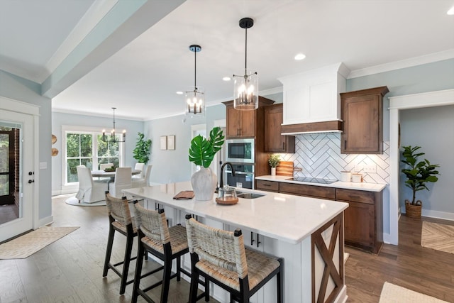 kitchen with backsplash, a breakfast bar, sink, decorative light fixtures, and an island with sink