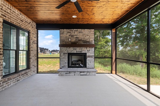 unfurnished sunroom with an outdoor stone fireplace, ceiling fan, and wooden ceiling