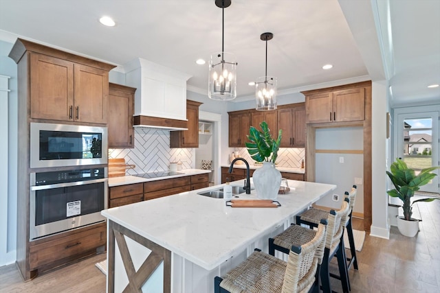 kitchen featuring stainless steel oven, a center island with sink, black electric stovetop, sink, and tasteful backsplash