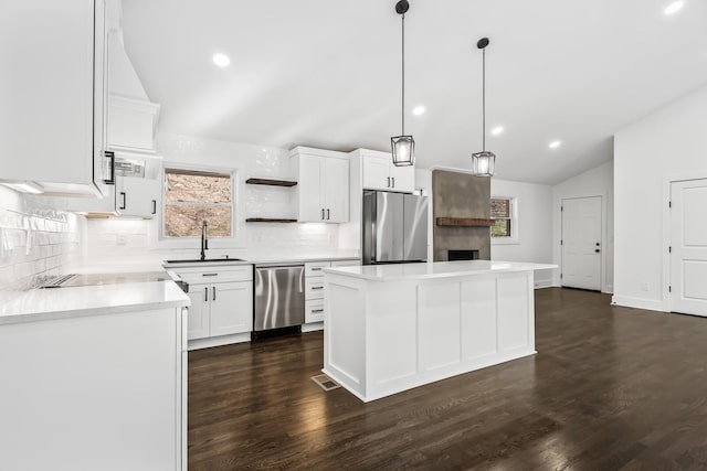 kitchen with appliances with stainless steel finishes, vaulted ceiling, a kitchen island, sink, and white cabinetry