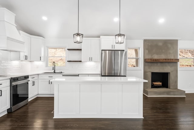 kitchen with stainless steel refrigerator, range with electric stovetop, pendant lighting, a kitchen island, and custom exhaust hood