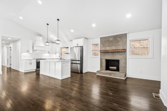 kitchen featuring stainless steel refrigerator, an island with sink, pendant lighting, white cabinets, and custom range hood