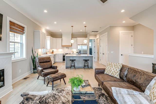 living room featuring crown molding, sink, a fireplace, and light hardwood / wood-style flooring