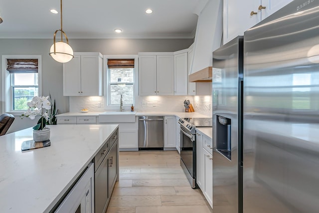 kitchen featuring appliances with stainless steel finishes, light stone counters, sink, decorative light fixtures, and white cabinetry