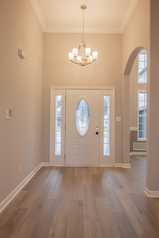 foyer entrance featuring a notable chandelier, a high ceiling, crown molding, and wood-type flooring