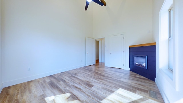 unfurnished living room featuring ceiling fan, light hardwood / wood-style flooring, and a high ceiling