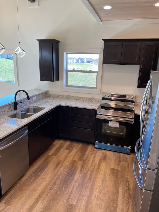 kitchen with hanging light fixtures, appliances with stainless steel finishes, sink, and light hardwood / wood-style floors