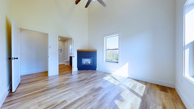 unfurnished living room with light hardwood / wood-style flooring, ceiling fan, and a high ceiling