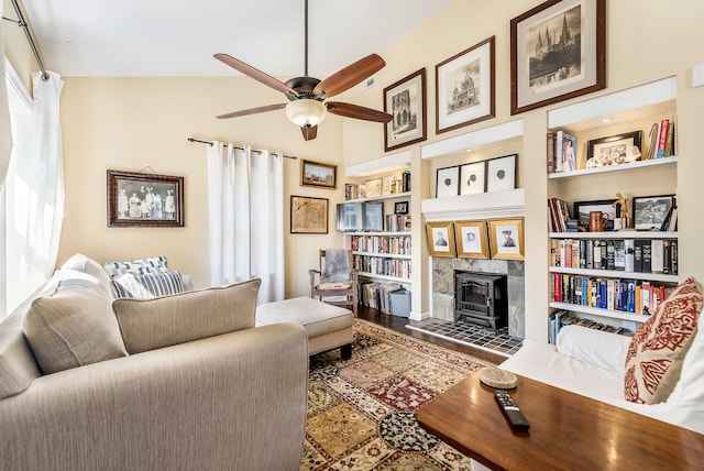 living area with built in features, ceiling fan, wood finished floors, a wood stove, and a healthy amount of sunlight