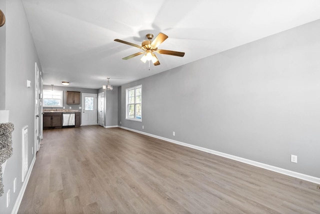 unfurnished living room featuring ceiling fan with notable chandelier, sink, and light wood-type flooring