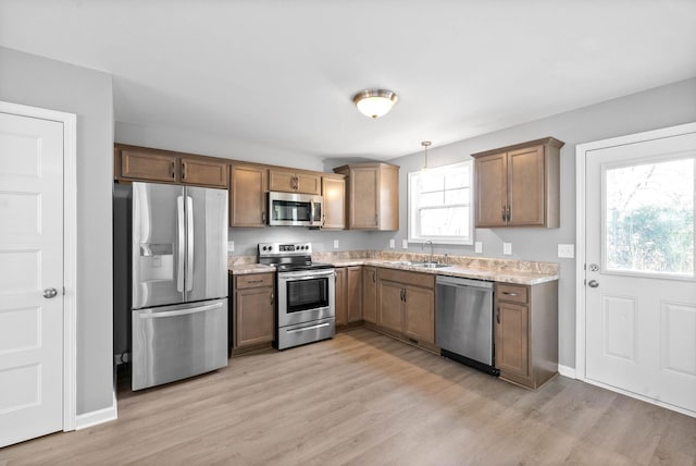 kitchen featuring light stone counters, light hardwood / wood-style flooring, decorative light fixtures, stainless steel appliances, and sink