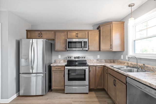 kitchen featuring decorative light fixtures, appliances with stainless steel finishes, light hardwood / wood-style floors, and sink