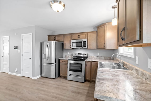 kitchen featuring stainless steel appliances, sink, hanging light fixtures, and light hardwood / wood-style flooring