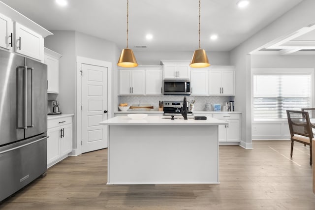 kitchen featuring stainless steel appliances, pendant lighting, an island with sink, and white cabinetry